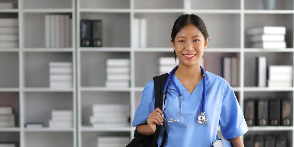 Nursing student smiling in library with bag over shoulder